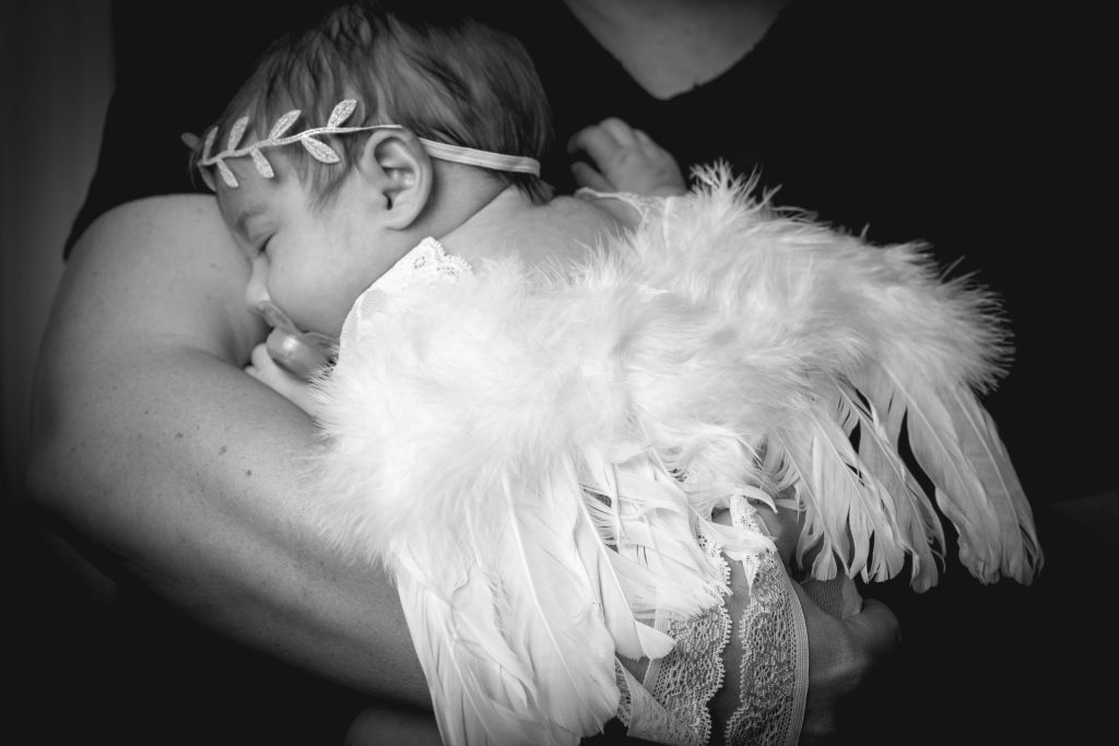 Bébé endormi déguisé en petit ange avec des ailes de plumes, blotti dans les bras d’un parent