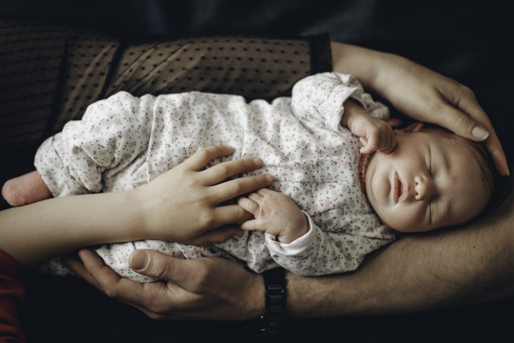 Nouveau-né endormi allongé dans les bras croisés de ses parents pendant une séance photo naissance