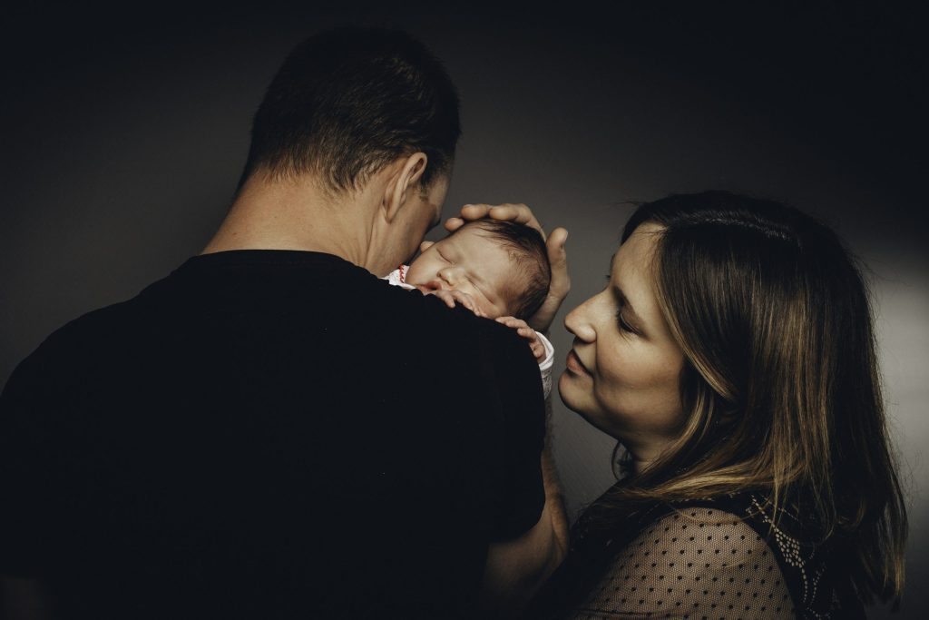 Jeunes parents avec leur nouveau-né, le père porte le bébé contre son épaule et la mère le regarde tendrement.