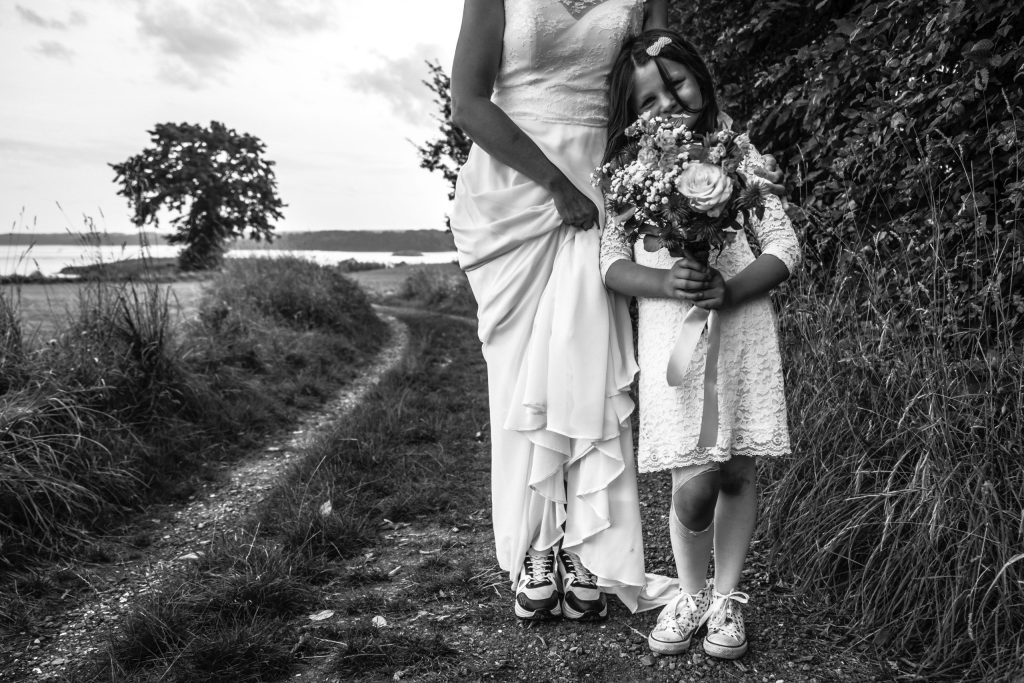 mariée en baskets aux côtés d’une petite fille tenant un bouquet, sur un chemin de campagne en noir et blanc