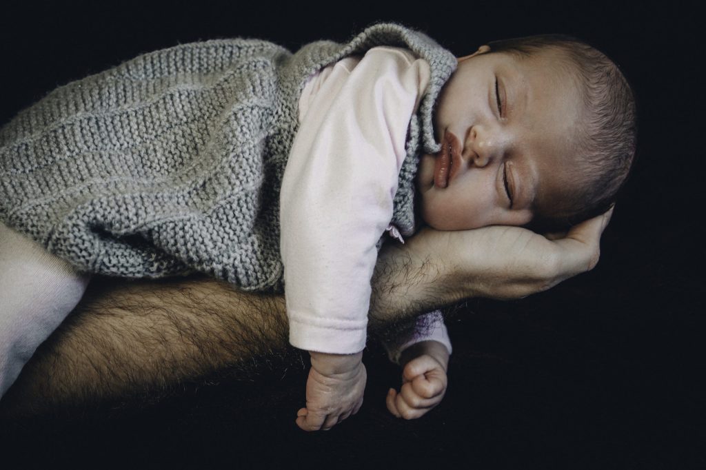Nouveau-né endormi dans le bras d’un parent, photographie de naissance en lumière douce.