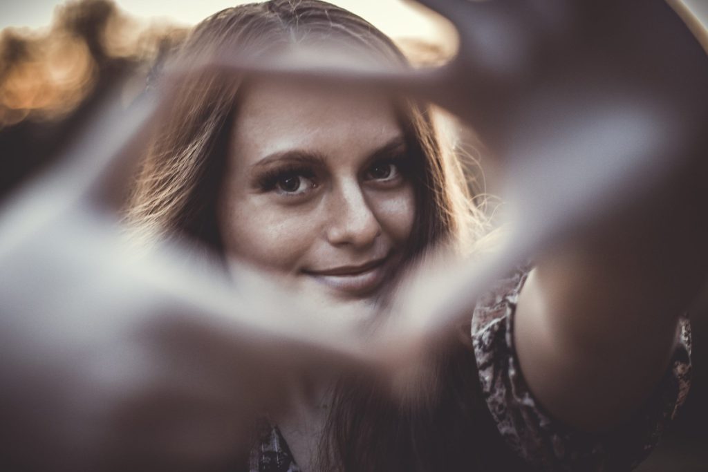 Une jeune femme qui regarde l'objectif en faisant un carré avec sa main.