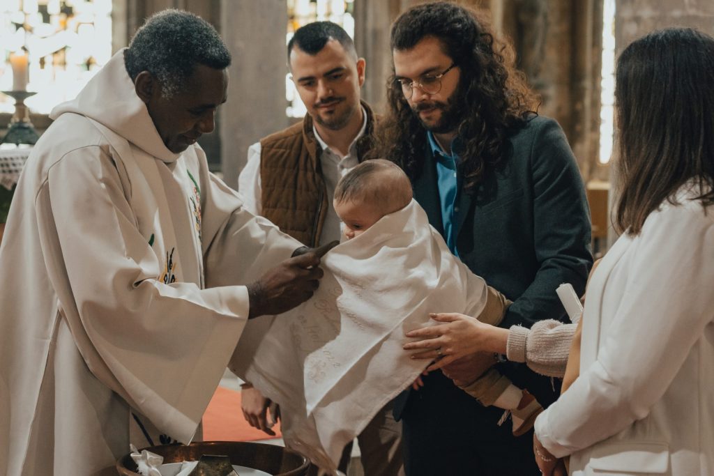 Baptême d’un bébé à l’église, prêtre et parents réunis autour de l’enfant – reportage de cérémonie.