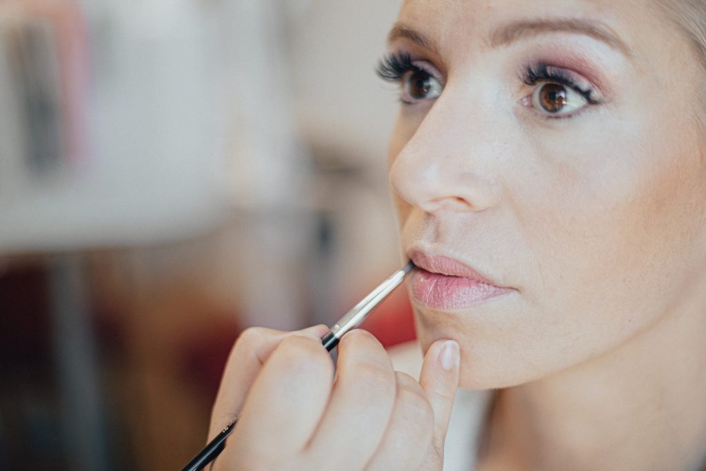 Maquillage de la mariée, pinceau posé sur les lèvres pendant les préparatifs du mariage.