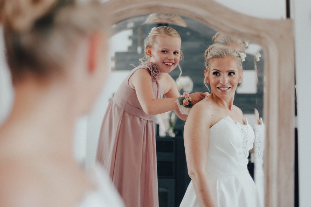 Mariée et petite demoiselle d’honneur se préparant devant un miroir, moments complices avant la cérémonie