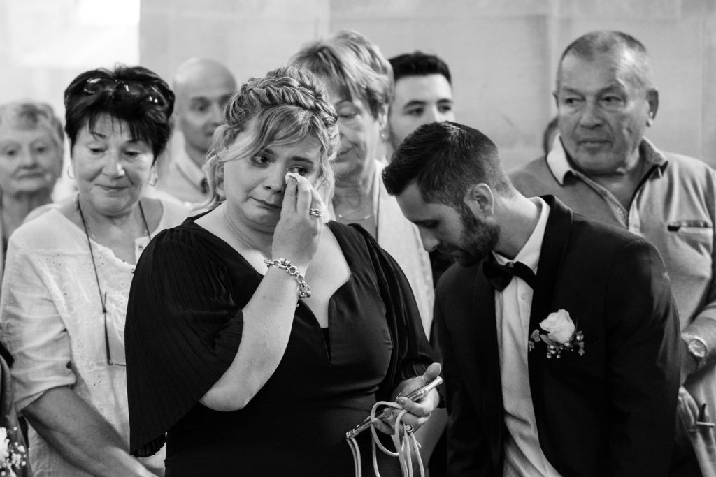 Émotion d’une maman essuyant une larme pendant la cérémonie de mariage, le marié à ses côtés.