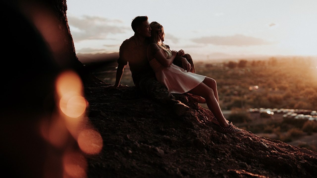 Couple enlacé l'un contre l'autre sur un mont et qui regarde un coucher de soleil.