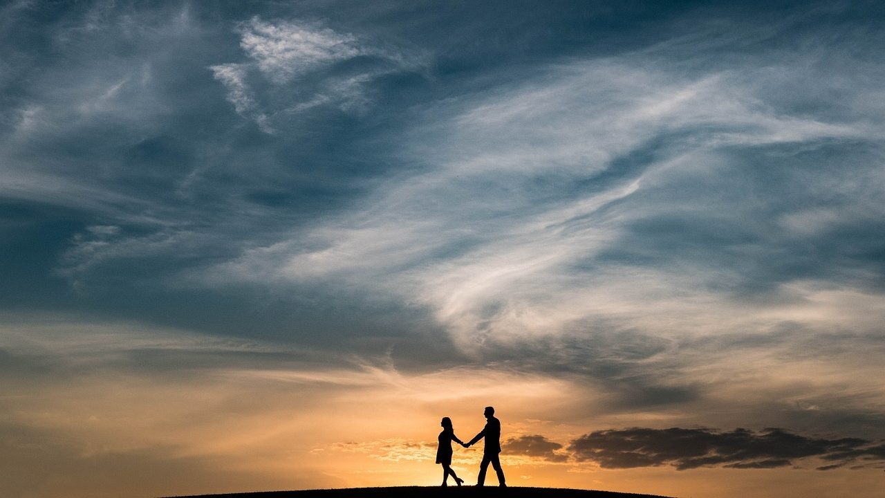 Couple qui se balade main dans la main dans la nature avec un coucher de soleil en arrière plan.