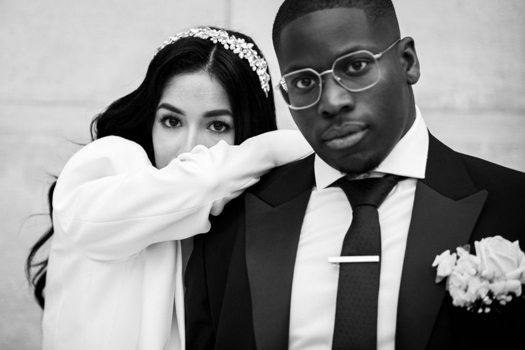 Portrait rapproché d’un couple de mariés, la mariée s’appuie sur l’épaule du marié, photo en noir et blanc au style éditorial.