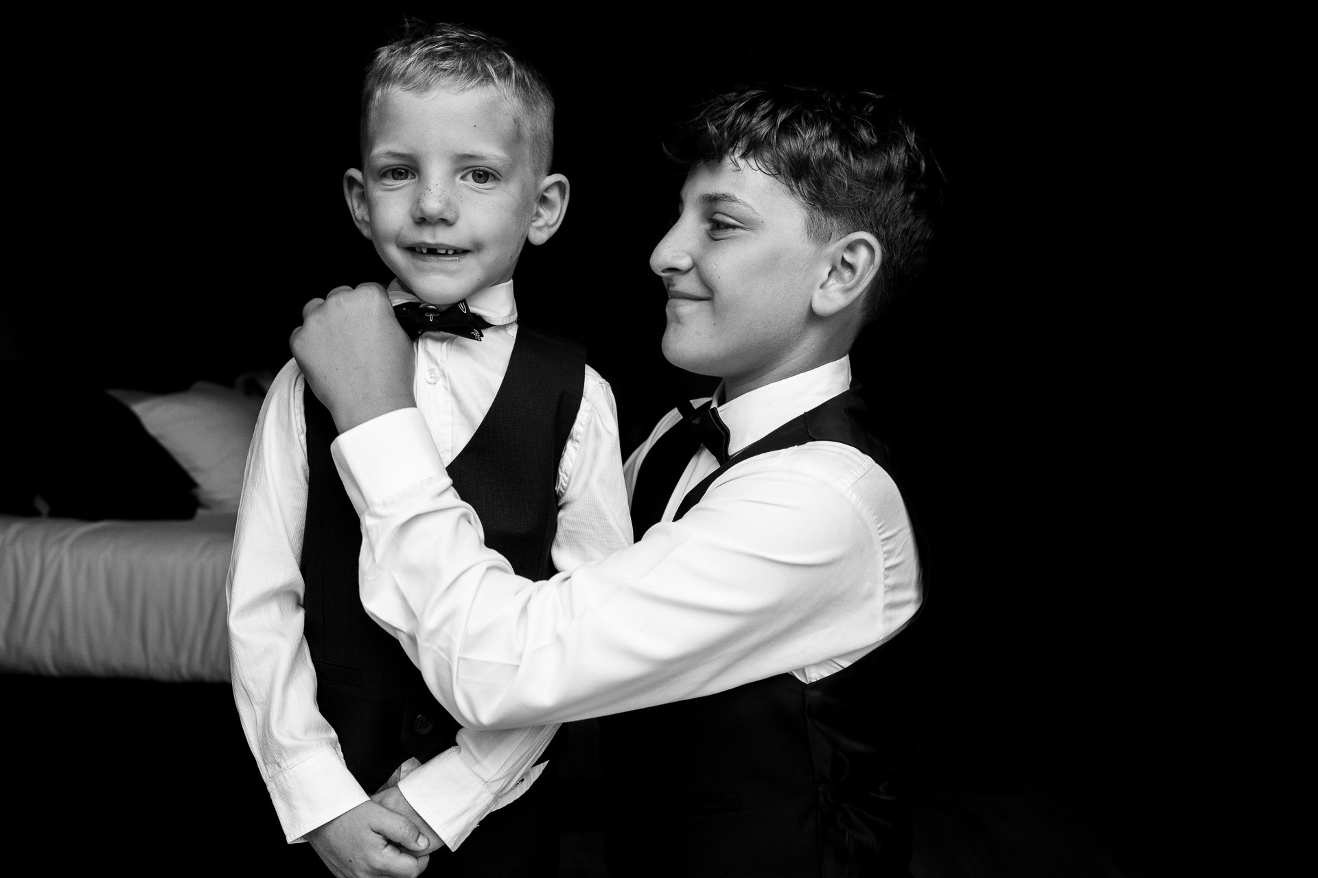 Deux garçons d’honneur en nœud papillon, le plus grand ajuste le nœud du plus jeune, portrait en noir et blanc lors d’un mariage.