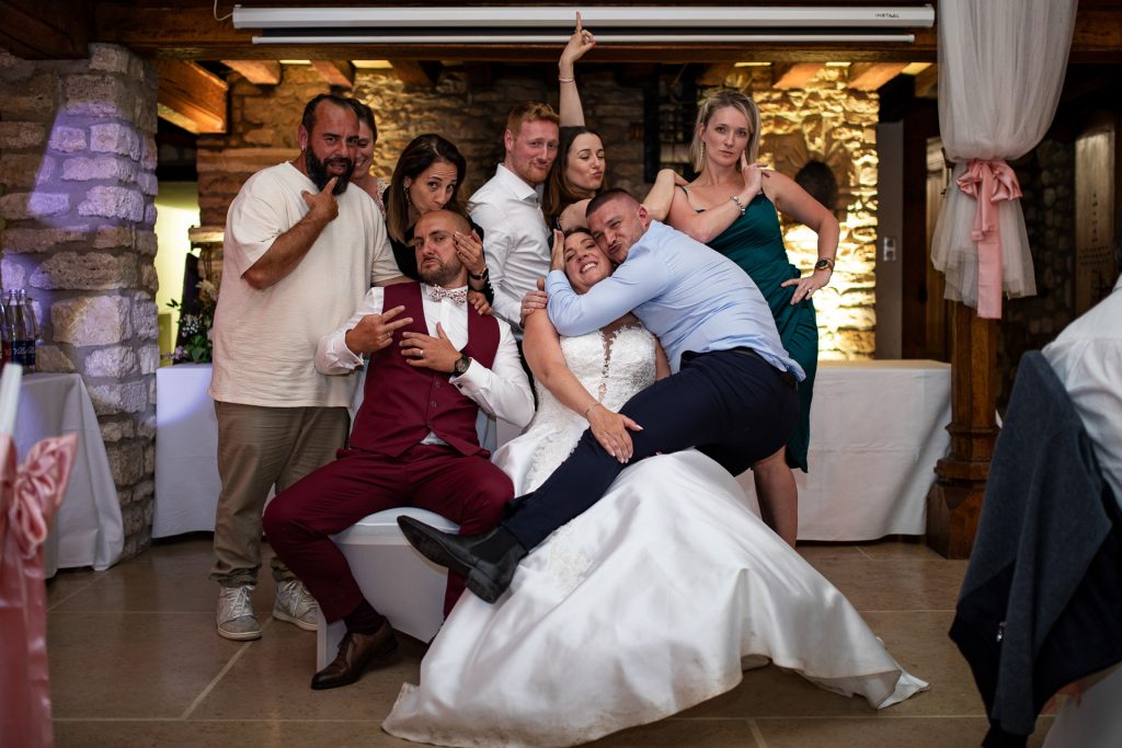 Photo de groupe festive en soirée de mariage, la mariée assise au centre entourée des invités qui posent de façon joyeuse.